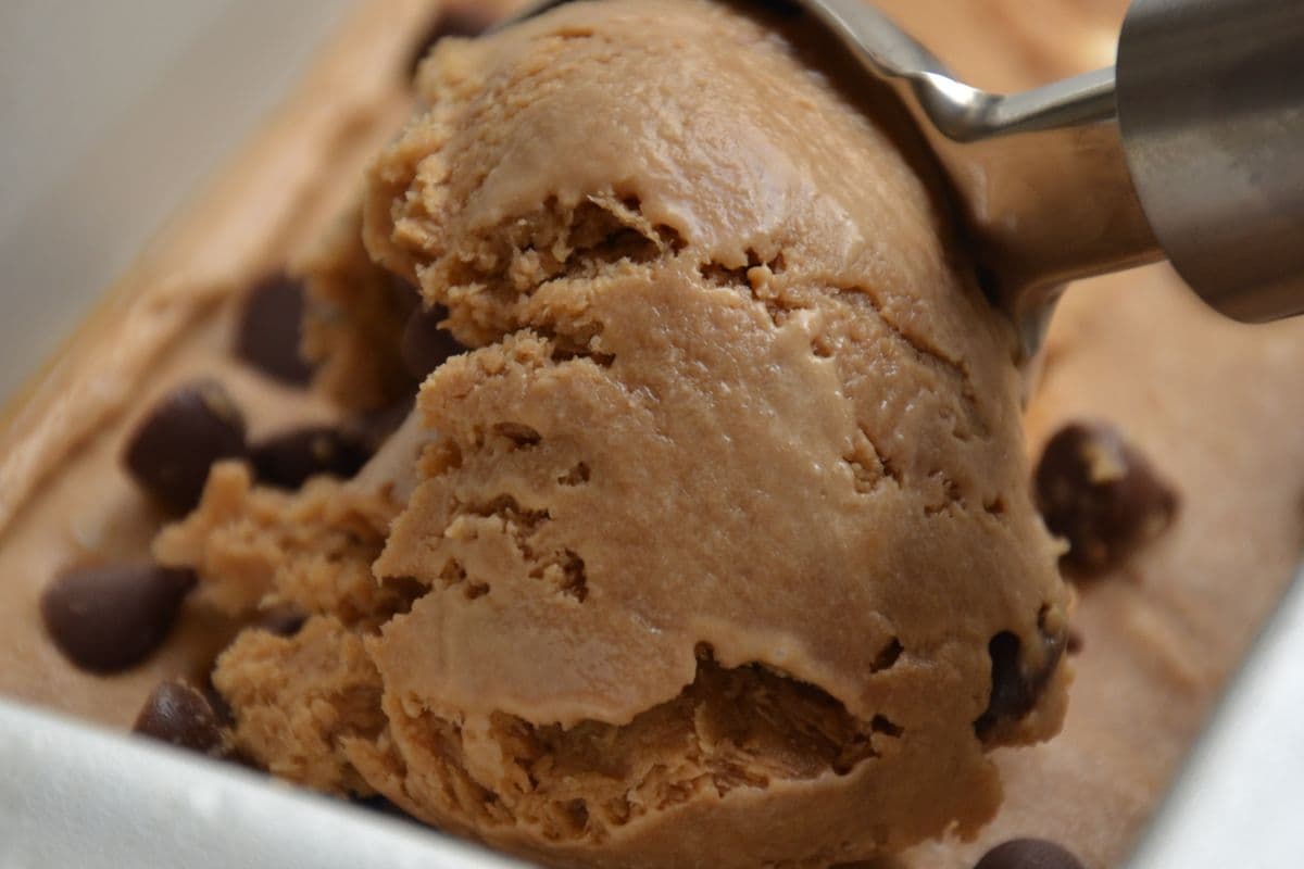 Close-up of a metal scoop lifting homemade chocolate chip ice cream out of a loaf pan